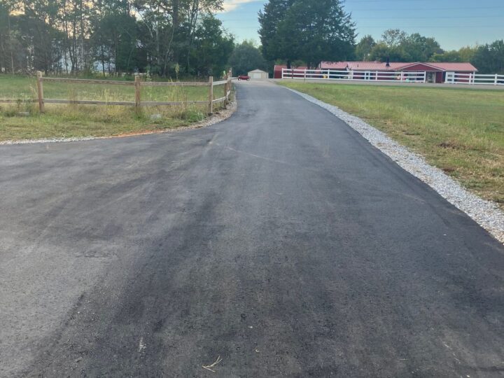 Long new asphalt driveway with a gravel edge and split-rail fence, after paving