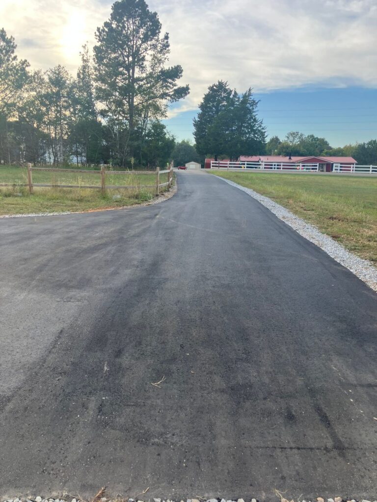 Long new asphalt driveway with a gravel edge and split-rail fence, after paving