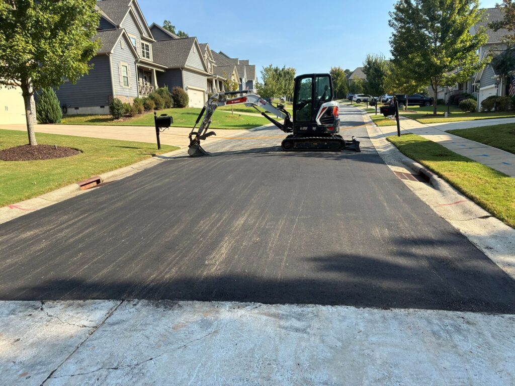 Fresh asphalt patch where a driveway meets a neighborhood street, with a Bobcat E35 mini excavator behind it