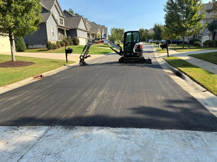 Fresh asphalt patch where a driveway meets a neighborhood street, with a Bobcat E35 mini excavator behind it