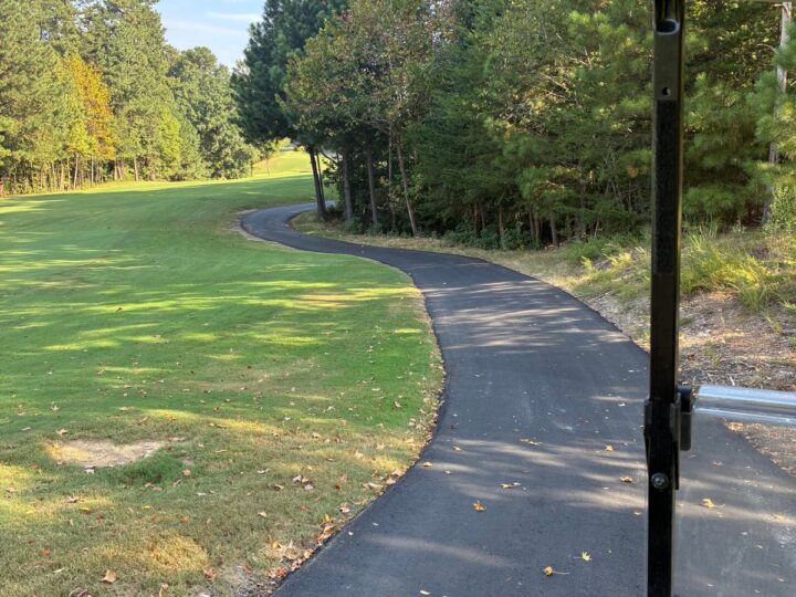 Newly paved asphalt golf cart path curving along a fairway, seen from a golf cart