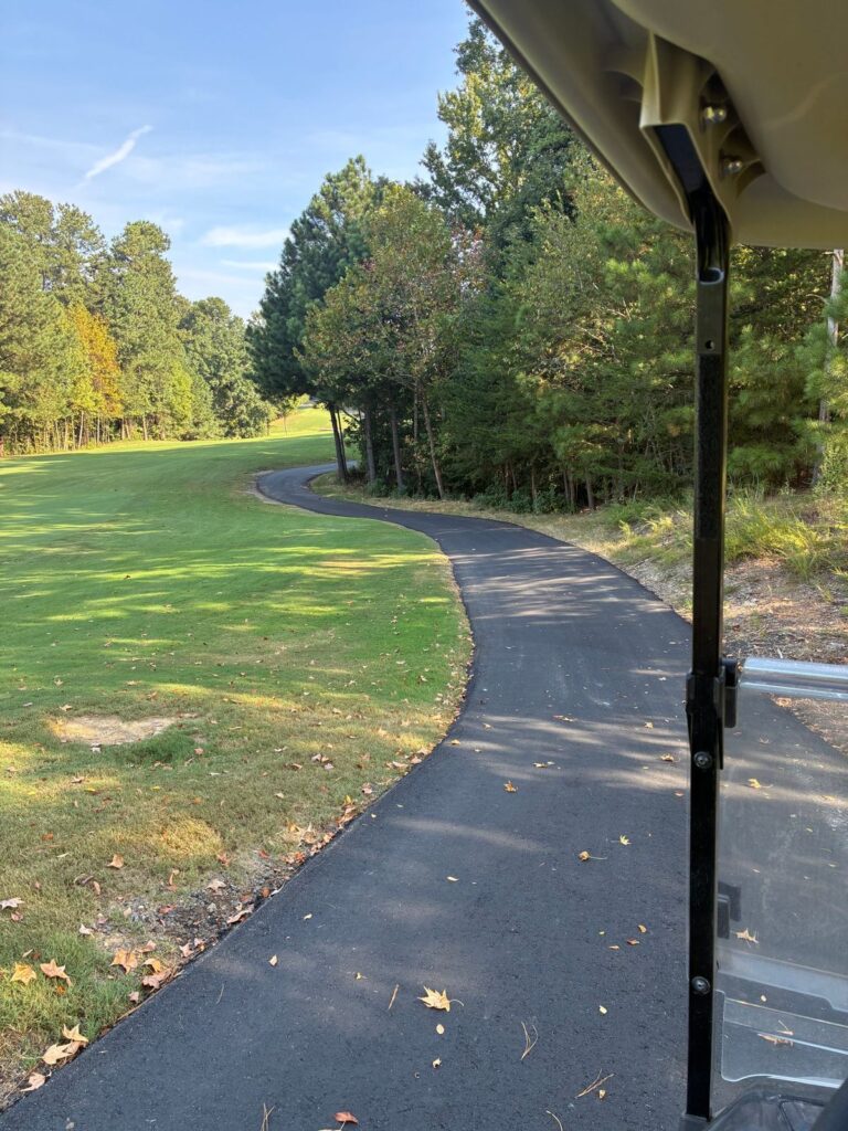 Newly paved asphalt golf cart path curving along a fairway, seen from a golf cart