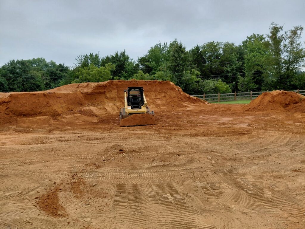 CAT skid steer grading a red clay lot with cut banks during site prep
