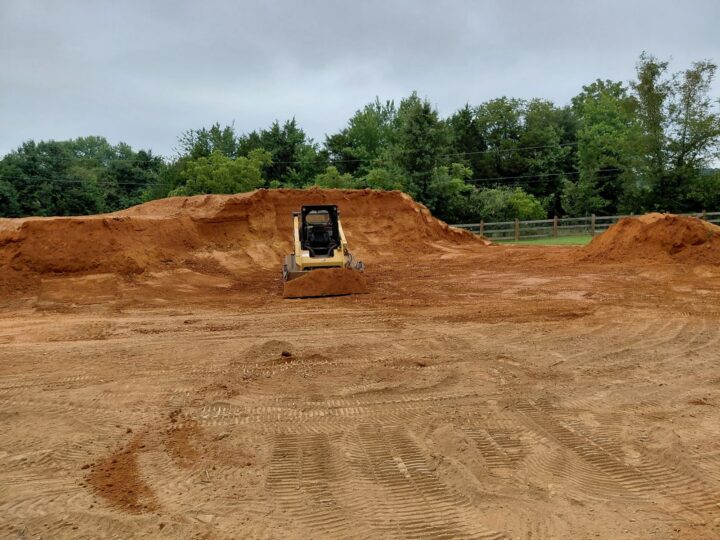 CAT skid steer grading a red clay lot with cut banks during site prep