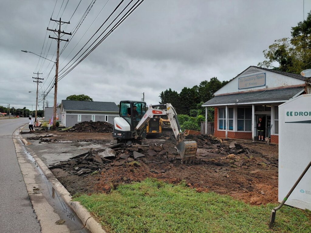 Mini excavator breaking up old asphalt in front of The Laundry Room of Stanley before repaving